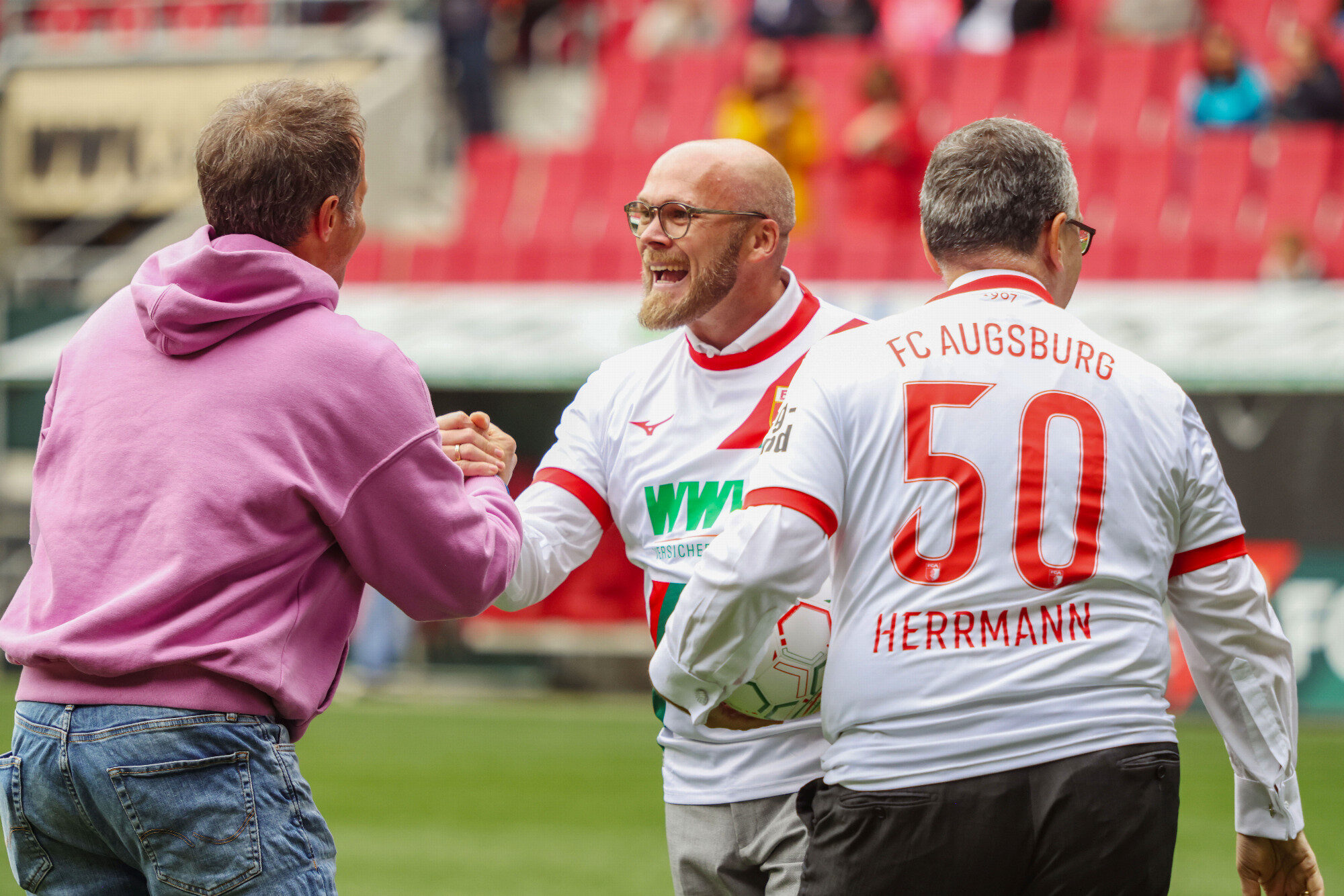 Handschlag auf dem Rasen vor dem Trikot „Herrmann 50“, WWK Arena Augsburg / Schulwerk
